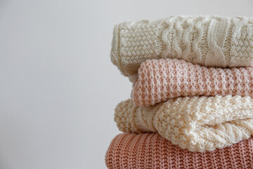 Bunch of knitted warm pastel color sweaters with different knitting patterns folded in stack, clearly visible texture. Stylish fall / winter season knitwear clothing. Close up, copy space for text.