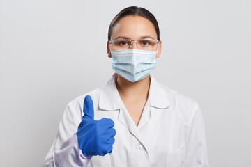 Woman doctor in protective mask and gloves shows thumb up gesture.