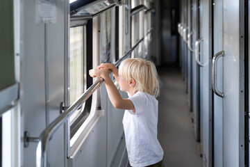 Blond boy in railway carriage. Handsome kid looking out of train window