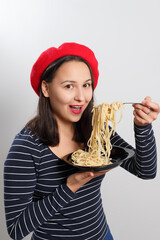 Young woman in a red beret eating spaghetti. On white.