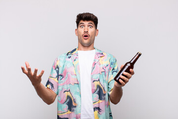 young man with a beer open-mouthed and amazed, shocked and astonished with an unbelievable surprise
