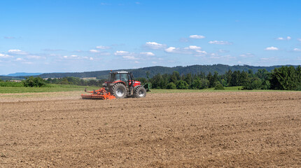 Traktor eggt ein landwirtschaftliches Feld aus brauner Erde in idyllischer Landschaft