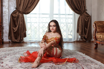 beautiful young girl in traditional belly dancer costume red color. sitting on the floor and looking straight