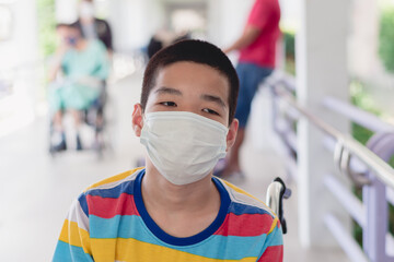 Asian special child on wheelchair wearing a protection mask against PM 2.5 air pollution and flu Covid 19 or Coronavirus on public path background, N95 to prevent the spread of the virus disease 2020.