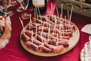 Side view of a round wooden plate with sliced and twisted pieces of meat on skewers. Catering.