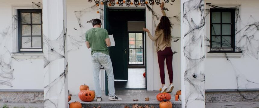 Caucasian couple of family decorating their house for Halloween celebration. Applying bat wall stickers. Shot on RED cinema camera with 2x Anamorphic lens