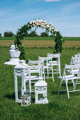 Round wedding arch decorated with peonies and greenery with white armchairs for guests outdoors