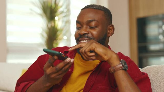 Happy african american young man recording voice message use phone in social network at sunlight. Talking smiling using wifi indoors communicate technology microphone speaker. Slow motion