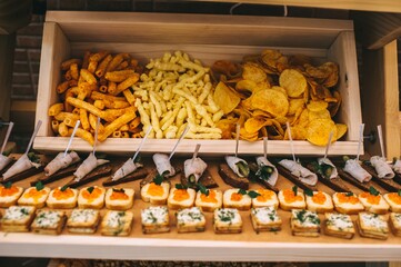 Different types of chips in a wooden box and a variety of canapes on the buffet table.