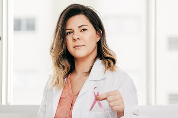 Healthcare and medicine concept - female doctor holding a pink breast cancer awareness ribbon