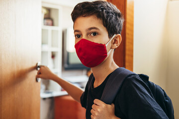 10 year old boy at home door with backpack and wearing face protection mask. Concept of back to...