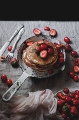 Pancakes in a frying pan garnished with cherries and strawberries