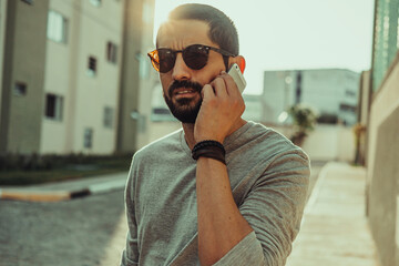 Young casual man using smartphone on the street. Wearing sunglasses, t-shirt and bracelets