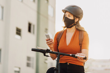 Young adult standing on bicycle using smartphone in the city wearing face mask against COVID-19