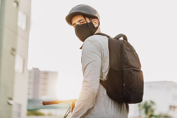 Young adult riding a bicycle through the city wearing face mask against COVID-19