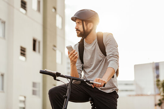 Young adult standing on bicycle using smartphone in the city