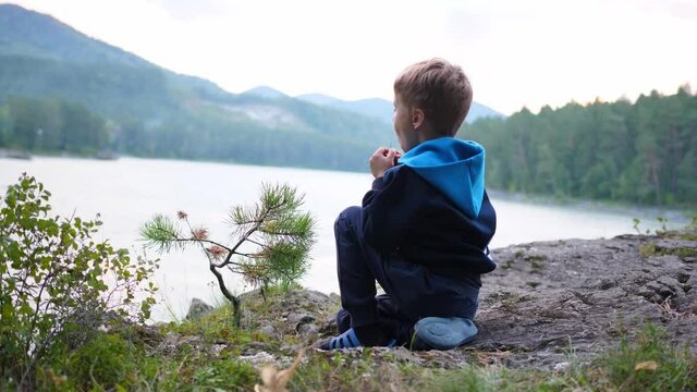 A child is sitting on the riverbank on a cliff. Evening time