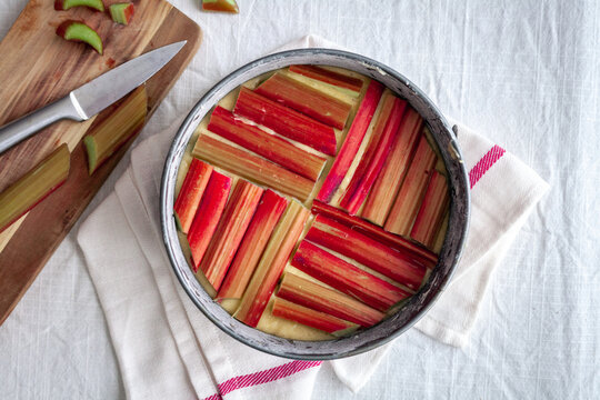 Top Down View Of A Rhubarb And Custard Pie On White And Red Cloth With Cutting Board And Knife And White Background