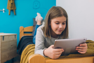 girl laying on bed and using tablet computer in her room 