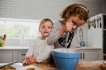 Two smiling siblings baking together in kitchen.
