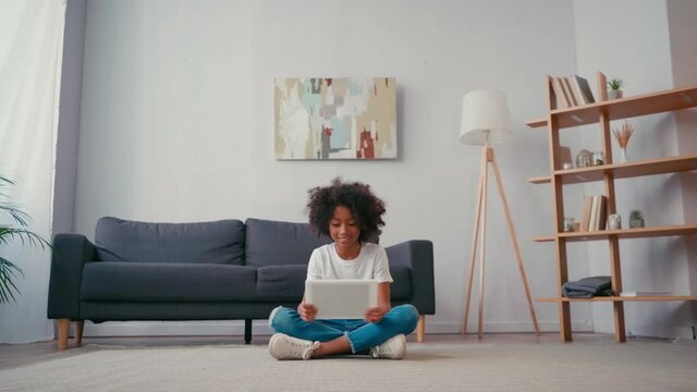 African american girl with crossed legs using digital tablet at home