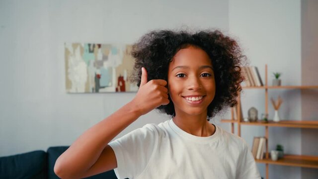 Selective focus of african american girl with thumb up looking at camera at home