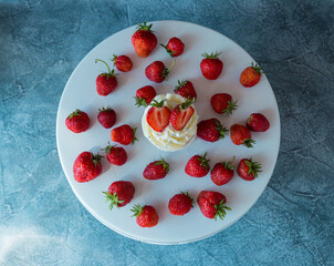 cupcake in the center with white cream decorated with ripe strawberries on a gray blue background and scattered strawberries.