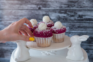Female hand takes from the stand a delicious cupcake with violet cream decorated with balls topped with coconut crumbs