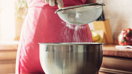 A girl sifts flour through a sieve before preparing a cake in the kitchen.