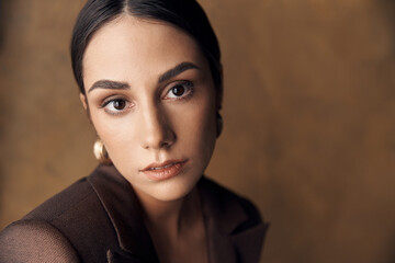 portrait photo of a beautiful stylish girl in a brown suit,on brown background in studio, she mysteriously looks into the camera with her brown eyes