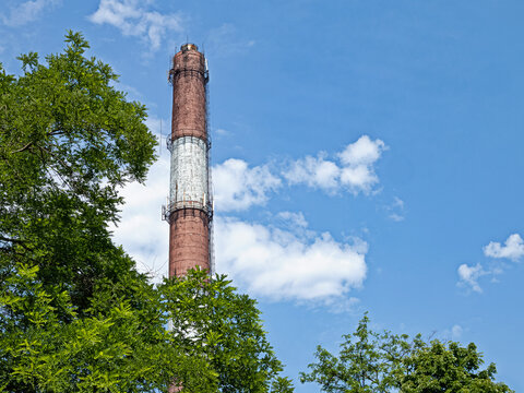 A High Chimney Rises into The Blue Sky Against the Backdrop of Running Snow-White Clouds
