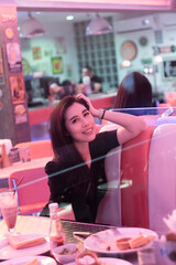 Young beautiful retro girl sitting in a diner restaurant. Woman in black eating in a diner with beautiful neon light. Pretty happy young woman sitting in the diner. Fashion girl in a vintage cafe.