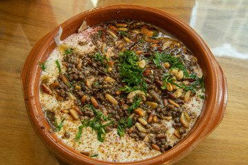 Traditional Levantine ‘fatteh’ dish made of flatbread covered with minced meat, tahina, pine and cashew nuts and strained yogurt and topped with sizzling butter and fresh herbs in Abu Dhabi