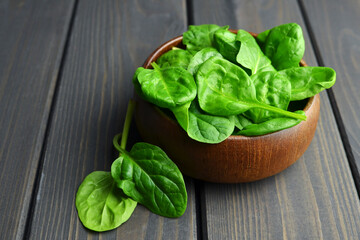 Spinach leaves in wooden bowl on dark background. Vegan food lifestyle concept.
