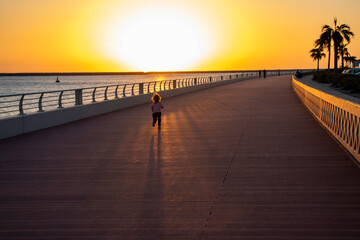 Little girl running on the boardwalk during sunset hour.