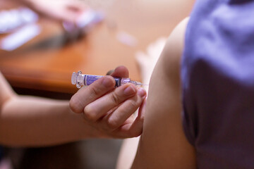 Close up of doctor giving an injection to young woman. Doctor give injection to patient's arm at home doing quarantine. Doctor giving a vaccination shot to a young woman at home.