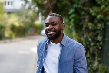 Fototapeta premium Close up portrait of a happy African American man. Handsome young man in blue denim shirt walking in the street and smiling.