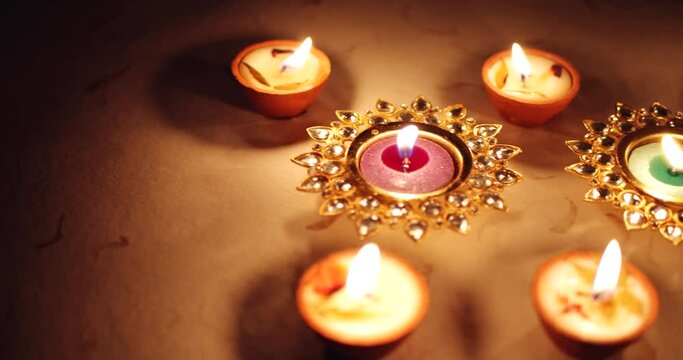 Pan right to Beautiful tabletop flat-lay view of multiple earthen handmade and crystal metal Diyas wax candles burning bright for decoration for Diwali- Hindu festival of lights, India on petal base 