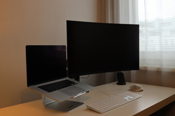 Moderner Home Office Arbeitsplatz mit einem großen gebogenen Monitor, der zu schweben scheint, und einem neuen und grauen Laptop.