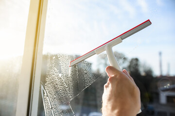 Glass cleaner with a squeegee for cleaning windows, blue sky. The person holds a squeegee in his hand and washes the detergent from the window. Selective focus, blur