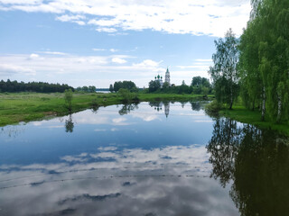 Fototapeta na wymiar a small river in it clouds are reflected on the bank of a small village church