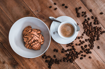 cup of espresso accompanied by cookies with chocolate on a white plate, coffee beans on a rustic wooden background, top view