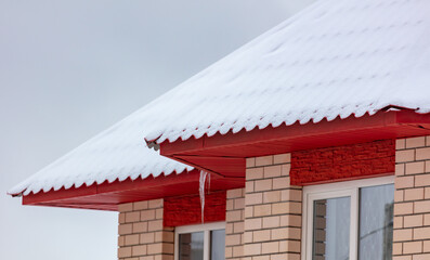 White snow lies on the red roof of the house.
