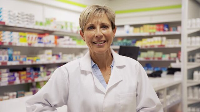 Female pharmacist standing smiling leaning happily against counter in pharmacy 