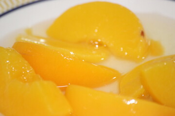 Canned peaches halves sprinkled with syrup in white plate.