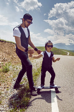 father teaches son to ride a black skateboard on the road