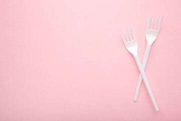 Two plastic forks on a pink background.