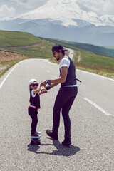father teaches son to ride a black skateboard on the road