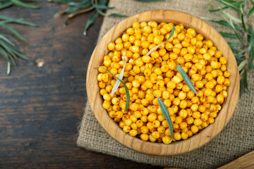 Sea buckthorn with leaves in a wooden bowl on a wooden table.
