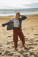 pretty young caucasian smiling woman wearing white blouse and denim jacket enjoying sun and fresh air on the beach  before sunset. Image with selective focus